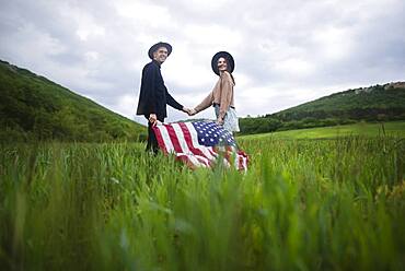 Young couple with American flag holding hands in wheat field