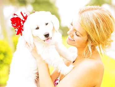 Young woman holding white puppy with ribbon bow, Jupiter, Florida