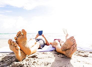 Close-up of sand-covered feet of young couple lying on blanket on beach reading, Jupiter, Florida