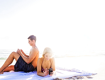 Portrait of young couple relaxing on beach, using smart phones, Jupiter, Florida