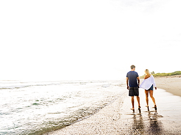 Young couple walking along surf line of sandy beach, holding hands, Jupiter, Florida