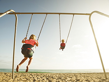 Girl (4-5) and boy (2-3) swinging on beach, San Clemente, California