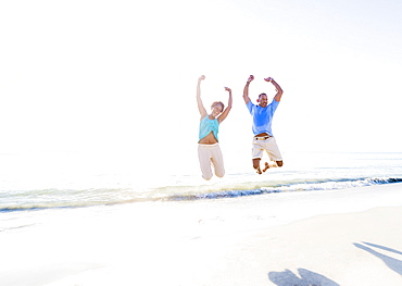 Mature couple jumping in sea with arms raised