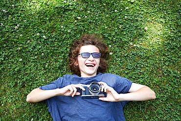 Boy lying in grass with camera