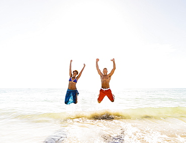 Mature couple jumping in sea with arms raised