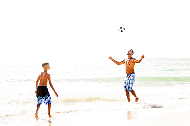 Father and son (10-11) playing soccer on beach
