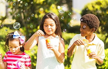 Girls( 4-5, 8-9) and boy (6-7) blowing soap bubble