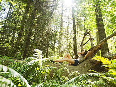 Young woman lying down on log, USA, Oregon, Portland