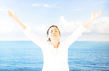 Portrait of woman with arms raised in front of backdrop with sea and sky