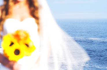 Mid section of bride holding sunflower bouquet, sea in background, USA, Maine, Bristol 