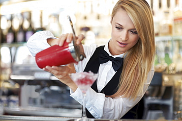 Young female bartender pouring cocktail 