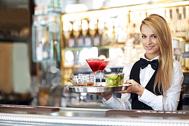 Portrait of female bartender holding tray with cocktails