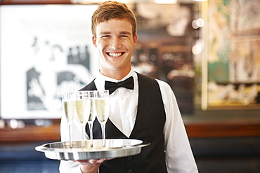 Portrait of waiter holding champagne flutes on tray