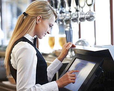 Young waitress using computer at restaurant counter