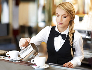 Female barista pouring milk into coffee cup