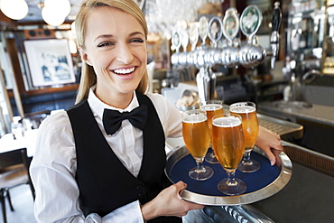 Portrait of young woman holding tray with beer glasses