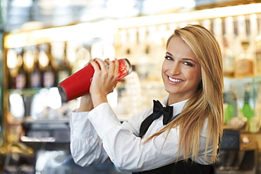 Young female bartender using cocktail shaker