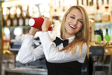 Young female bartender using cocktail shaker