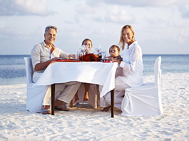 Portrait of parents with daughters (8-9), (4-5) sitting at table on beach, Thailand 