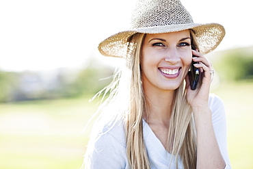 Portrait of smiling woman in straw hat using mobile phone