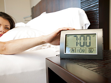 Young attractive woman turning off alarm clock