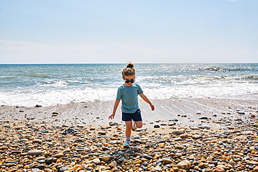 Girl (2-3) wearing sunglasses walking on pebbled beach