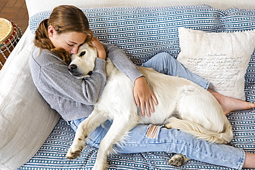 Girl (14-15) embracing English Cream Golden Retriever on sofa