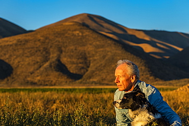 USA, Idaho, Bellevue, Senior man with border collie in field at sunset