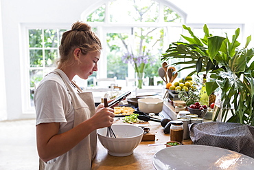 Girl (16-17) using phone while preparing meal in kitchen