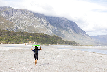 South Africa, Hermanus, Boy (8-9) carrying bodyboard on beach