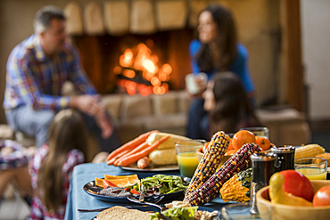 Dinner on table and family with children (10-11, 12-13, 16-17) sitting by fireplace