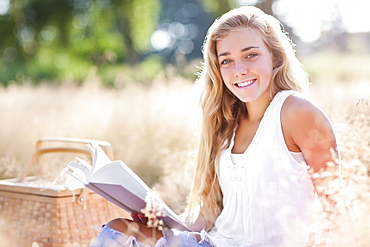 Teenage girl (16-17) posing for portrait while reading book outdoors