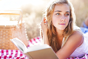 Teenage girl (16-17) taking break from reading book outdoors