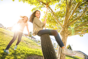 Girls (10-11, 12-13) playing with tire swing in garden