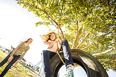 Smiling girls (10-11, 12-13) on tire swing in garden