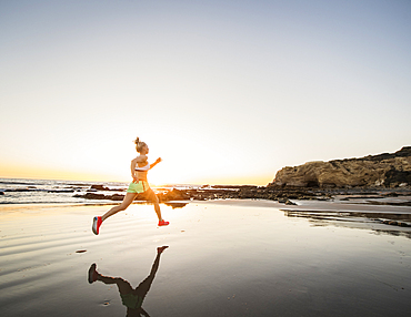 United States, California, Laguna Beach, Rear view of athlete woman running on beach at sunset