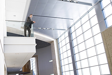 Businessman leaning on balcony in building lobby