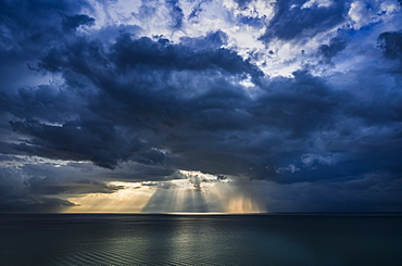 Sun rays shining onto ocean below large cumulus storm clouds