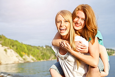 Portrait of two young women piggy-backing on beach