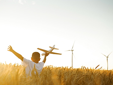 Boy (10-11) playing with toy aeroplane in wheat field