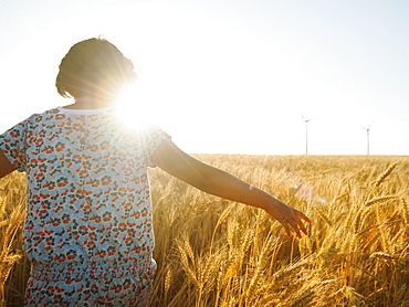 Girl (10-11) walking in glorious sunshine amidst wheat