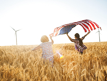 Girls (10-11, 12-13) flying american flag in wheat field