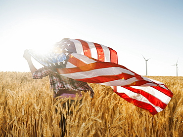 Girl (12-13) flying american flag in wheat field