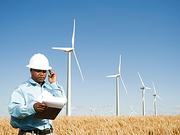 USA, Oregon, Wasco, Engineer standing in wheat field in front of wind turbines