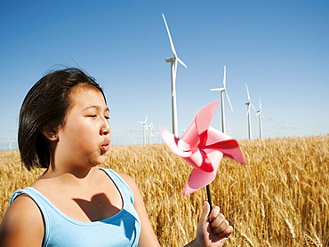 USA, Oregon, Wasco, Girl (10-11) holding blowing at fan in wheat field with wind turbines in background