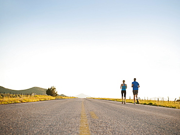 Mid adult couple running on empty road