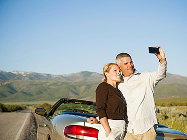 Mid adult couple photographing themselves in front of majestic mountain range