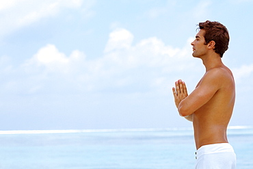 Smart young guy practicing yoga at beach