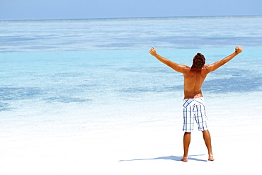 Man standing with his arms wide open on beach