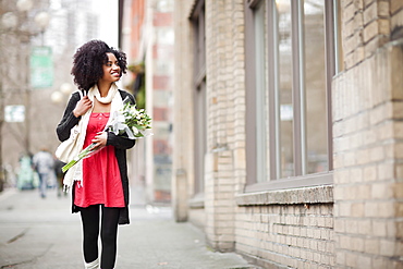 USA, Washington State, Seattle, Young woman walking in street carrying bunch of tulips